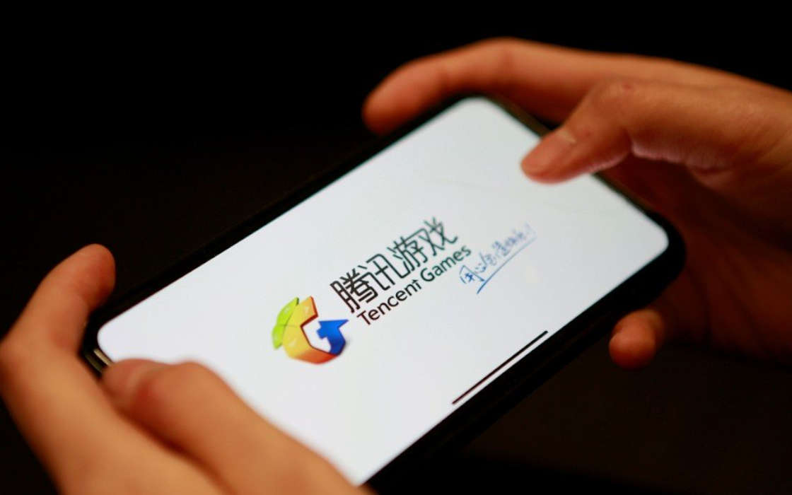 A player holding a phone with a Tencent Holdings game on it.